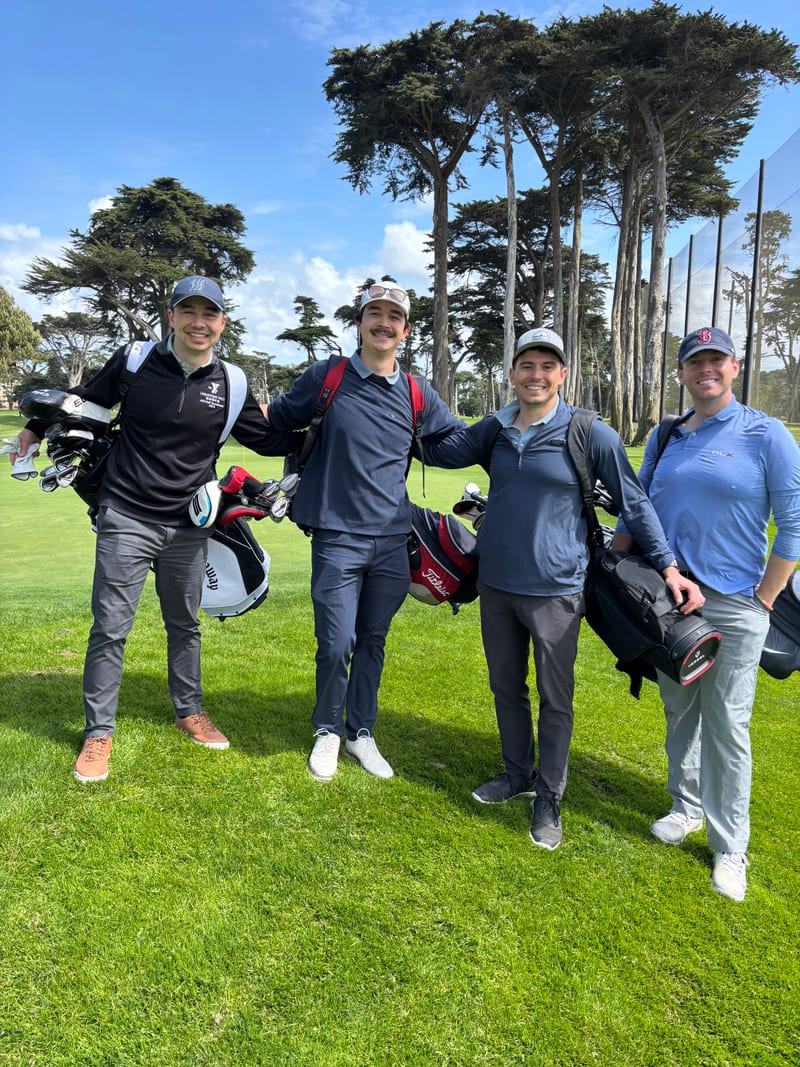 Scott and three friends carrying golf bags on a fairway lined with cypress trees