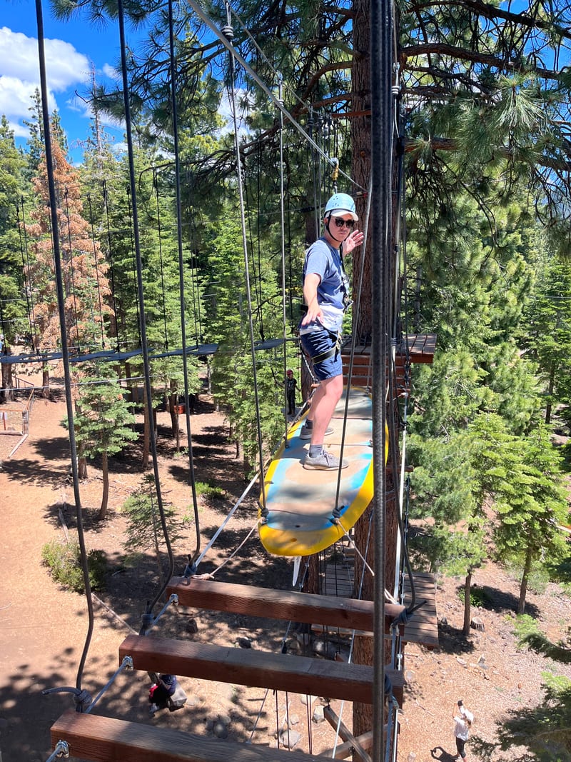 Scott balancing on a suspended paddleboard at a treetop ropes course