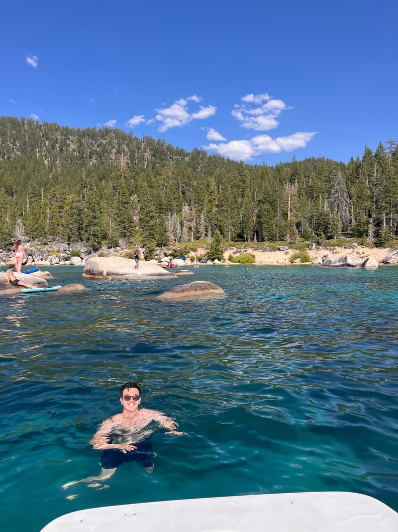 Scott swimming in the clear turquoise water of Lake Tahoe, pines and granite boulders behind