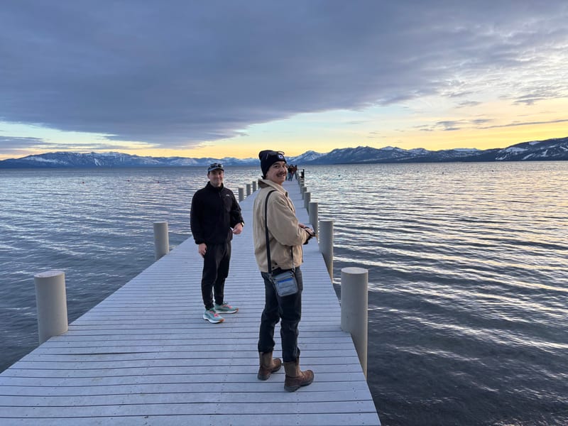 Scott and a friend on a pier at Lake Tahoe at sunset, snowy mountains across the water